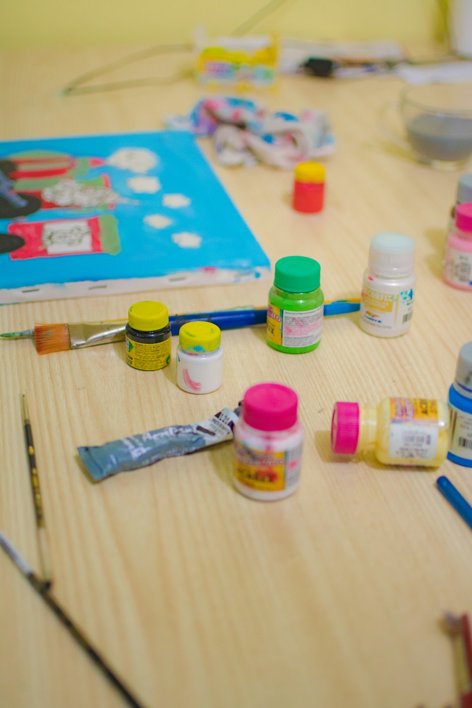 Art supplies arranged around an unfinished blue canvas on a wooden table.