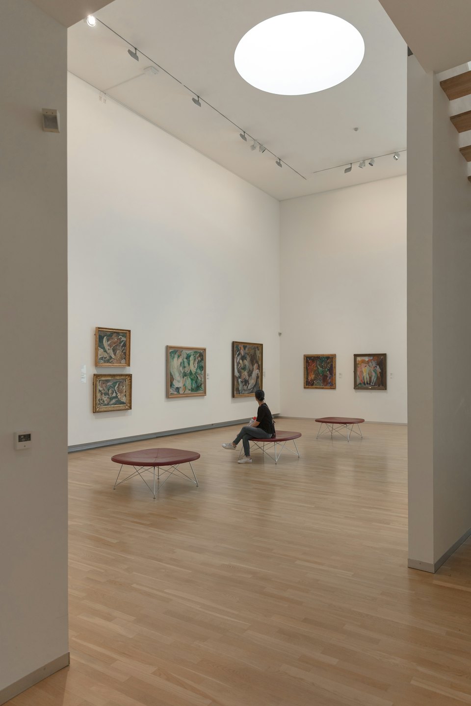 Person sits on bench looking at artwork in gallery.